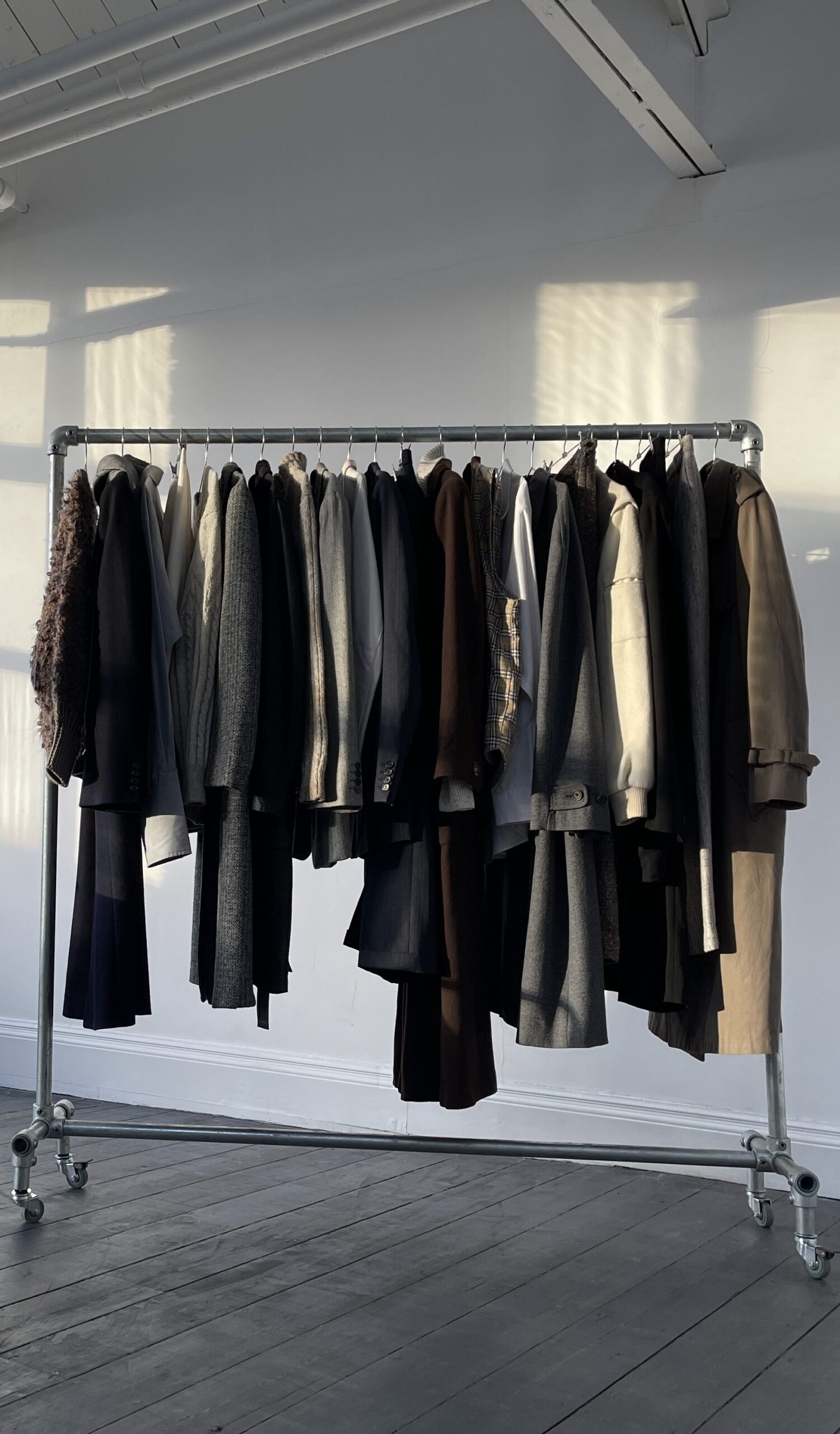 A number of clothing items hanging on a clothes rail, of assorted colours